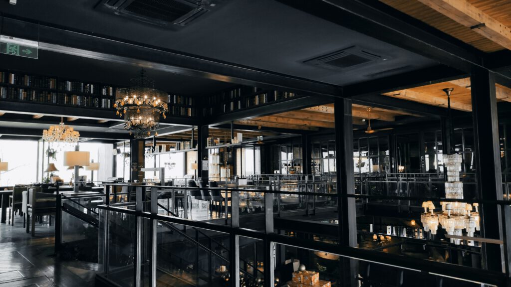 Elegantes, mehrstöckiges Restaurant oder Lounge mit dunkler Decke, luxuriösen Kronleuchtern und Glasgeländern, mit Blick auf Tische und Stühle.