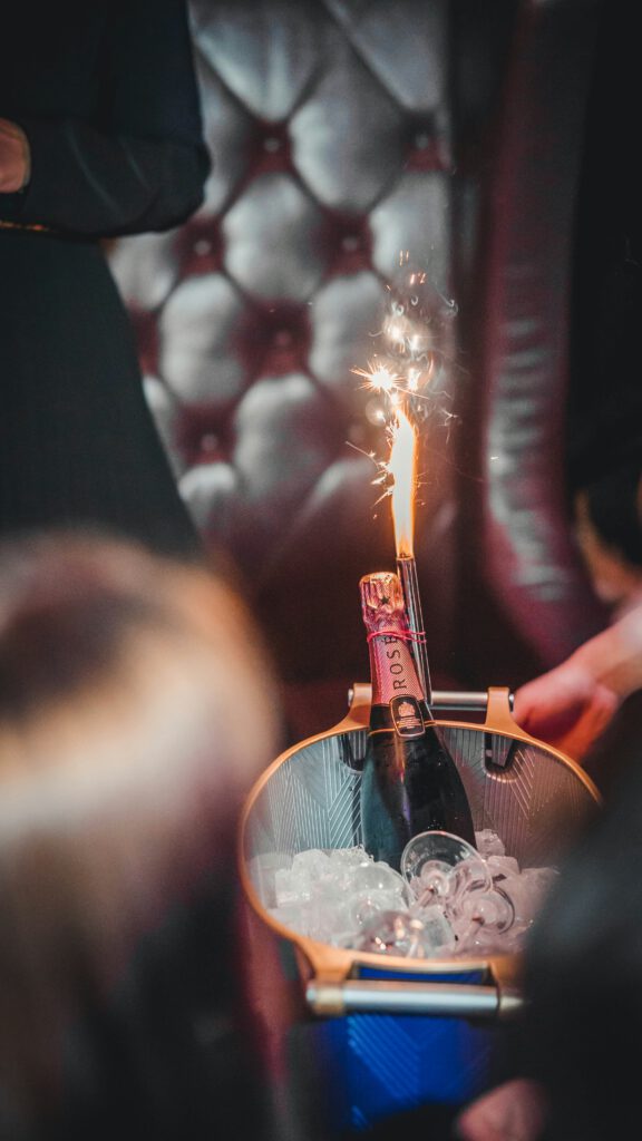 Nahaufnahme einer Flasche Rosé-Champagner in einem Eiskübel mit Wunderkerze in einer festlichen Atmosphäre.